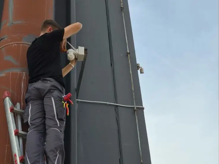 Električar na ljestvama montira kameru za videonadzor na fasadi objekta